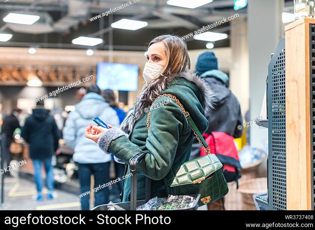 Woman standing in queue at cash desk in supermarket wearing mask keeping social distance