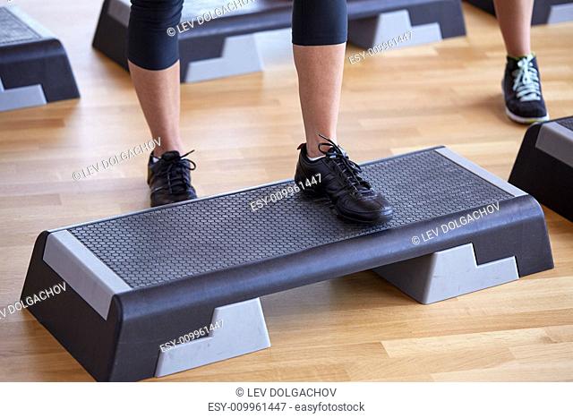 fitness, sport, people, step aerobics and lifestyle concept - close up of women legs exercising with steppers in gym