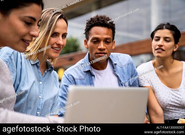 Diverse group of freelance contractor looking at a laptop's screen in an outdoors setting