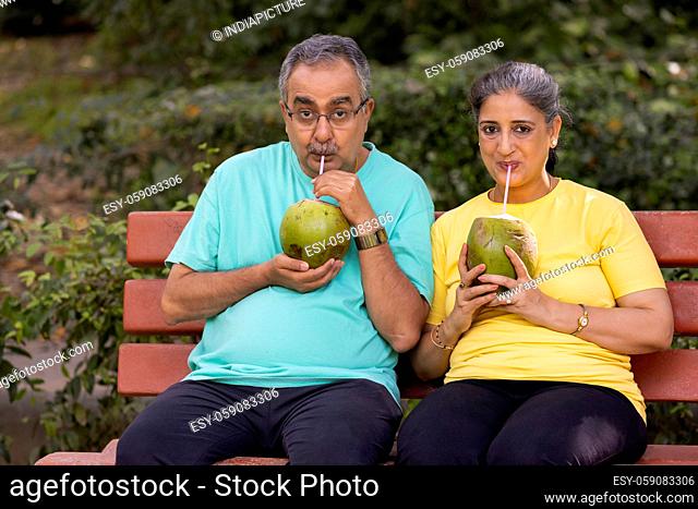 A SENIOR COUPLE SITTING IN PARK AND DRINKING COCONUT WATER