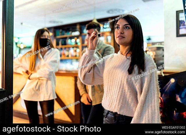 Young woman playing darts while friends standing behind in bar during COVID-19