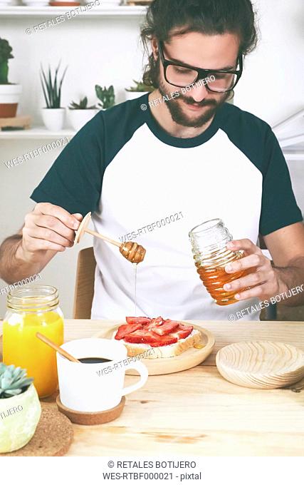 Young man putting honey on toast with strawberries