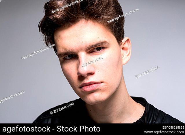 Wide angle. Studio shot. Young caucasian guy model in black clothes posing in the studio. Teenager in Leather Jacket Standing Against White Background