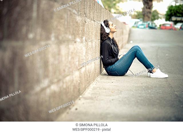 Teenage girl leaning against wall listening music with headphones