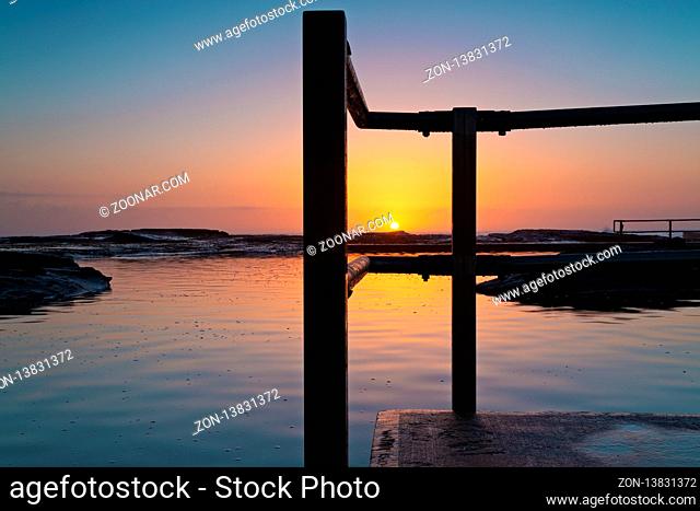 Glorious tranquil sunrise on the ocean horizon and ocean pool ripples and reflections. Location - North Curl Curl, nortthern beaches Sydney Australia