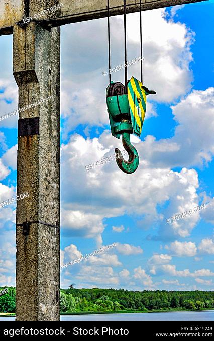 Yellow-green hook of a construction crane hanging on a rope on a background of clouds on a lake dam