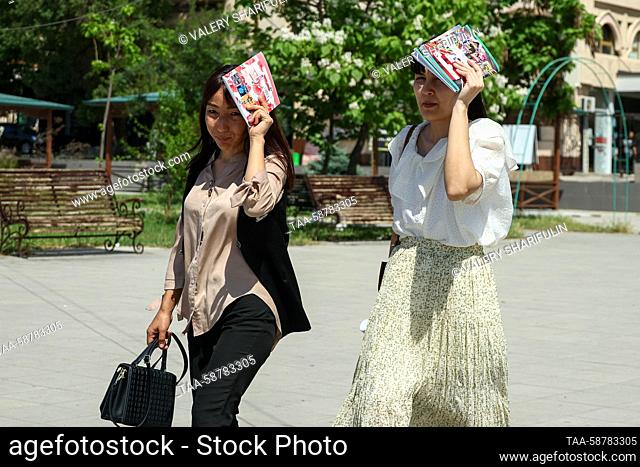 UZBEKISTAN, TASHKENT - MAY 1, 2023: Women cover their heads with copybooks as they walk in sunshine on a hot spring day. Valery Sharifulin/TASS