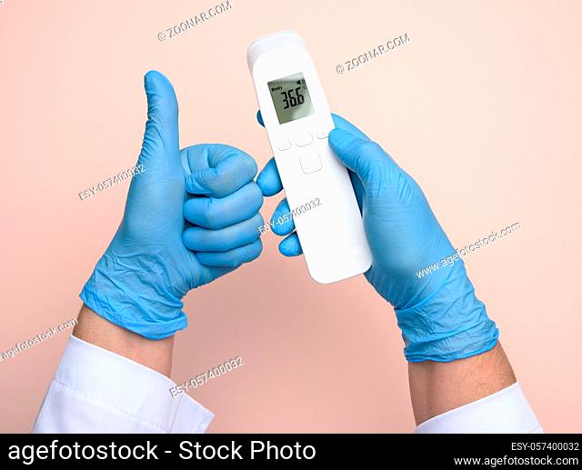 two hands in blue latex gloves hold an electronic thermometer to measure temperature, non-contact device