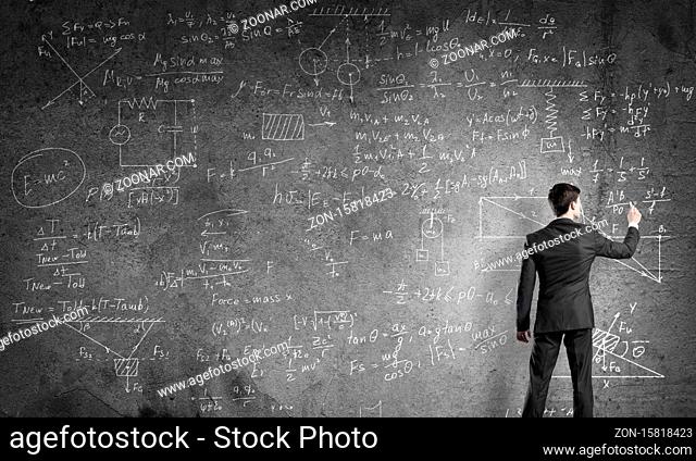 Man in suit standing with back and drawing physics formulas