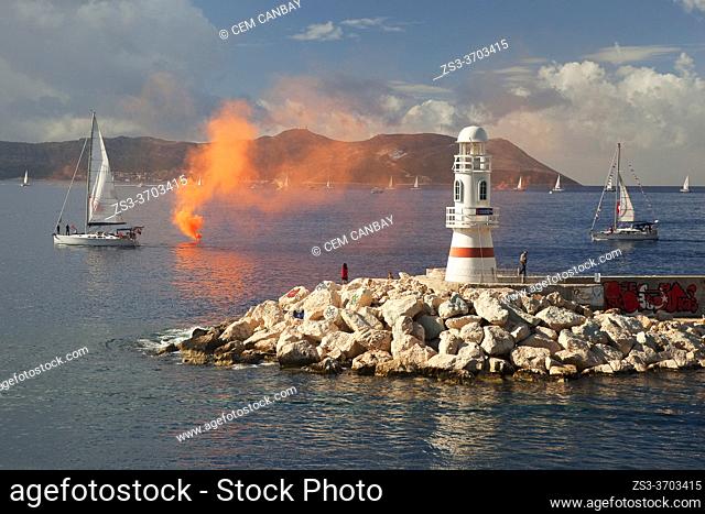 View to the people near the lighthouse taking photos of the parade of sailboats during the celebrations of the Independence day of Tukey at 29 October, Kas
