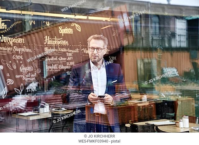 Mature businessman in cafe holding cell phone