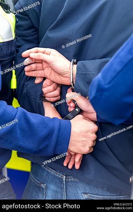 Illustration image shows a person being put in handcuffs during a photo opportunity with police vehicles and uniformed officers from the Antwerp Police Zone