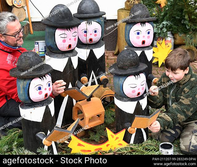 05 December 2021, Saxony, Borsdorf: Denny Pfaff (l) and his son Felix are repairing the chipped paint on the carol singers that decorate the Pfaff families'...