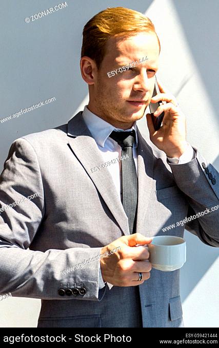 Portrait of a young business man talking on smartphone and holding cup of coffee