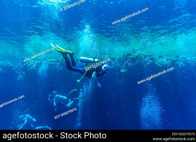 Front view on scuba divers group swimming who exploring deep dark ocean blue water against the backdrop of a coral reef. Male and female in flippers examines...