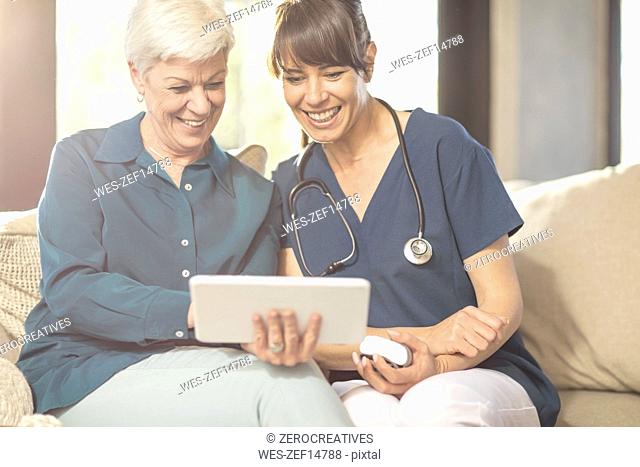 Senior woman sharing tablet with nurse at home