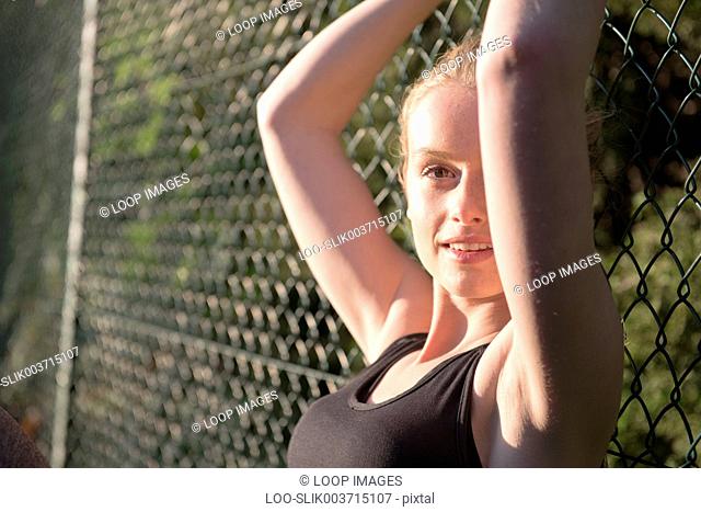 A young woman enjoying the evening sunshine sat on a tennis court