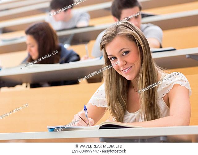 Woman sitting at the lecture hall while smiling and writing notes