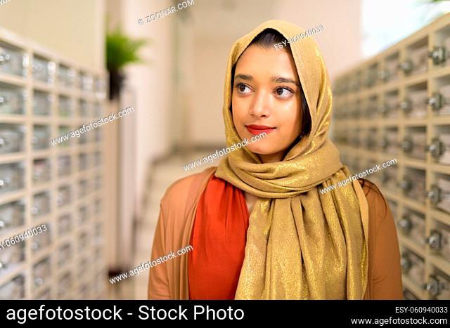 Portrait of young beautiful Indian Muslim woman with hijab at the mailbox of modern building