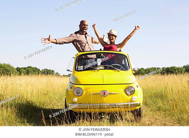 Couple standing in car sun roof in field