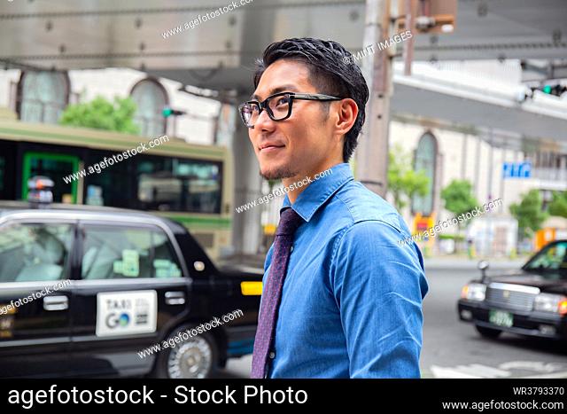 A young businessman in the city, on the move, a man in a blue shirt and tie, a taxi behind him