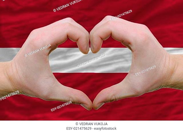 Heart and love gesture showed by hands over flag of latvia backg