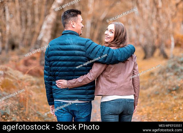 Happy couple with arms around walking in Cannock Chase park during autumn