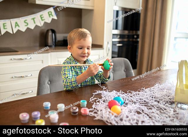 Concentrated busy cute child dyeing the surface of an eggshell with green food coloring