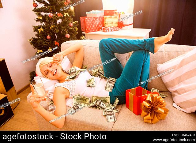 Happy Christmas woman lying on sofa or couch, drinking champagne and smiling from receiving New Year gift or present from Santa Clause