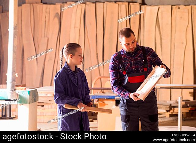 Professional carpenter teaches young teen boy to plain wood in a carpentry workshop. Boy and man at the workshop, wooden planks on bakground