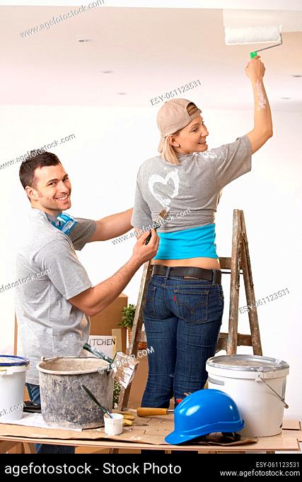 Smiling woman painting the ceiling standing on ladder, laughing guy painting heart on tshirt
