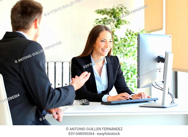 Agent attending to a client introducing data in a desktop computer at office
