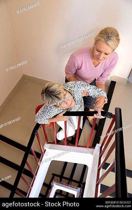 Elderly woman being helped by another woman to climb the stairs