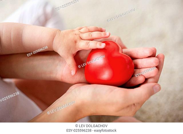 family, charity and people concept - close up of little baby and mother hands holding red heart