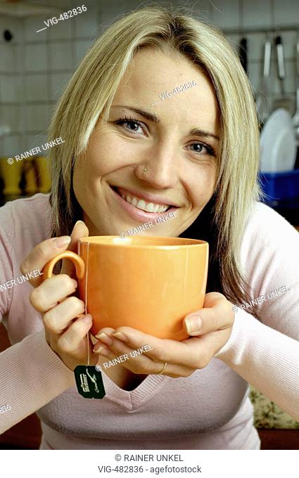 GERMANY : Young woman drinking a cup of tea in her kitchen . - Koeln, GERMANY, 24/07/2007