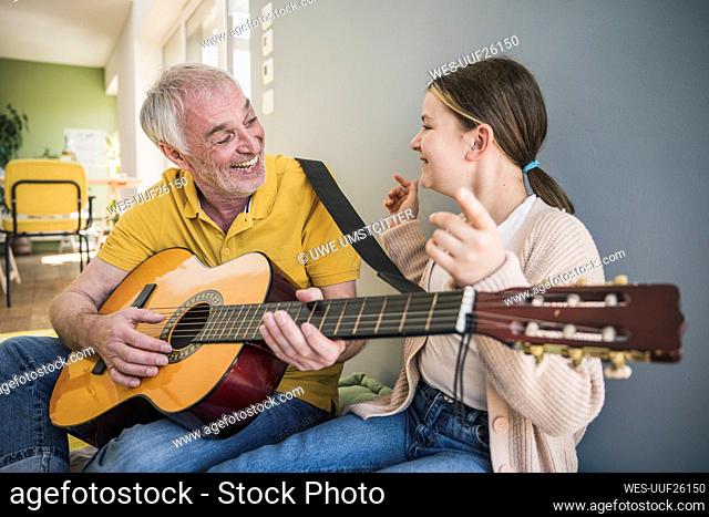 Happy senior man playing guitar by granddaughter at home