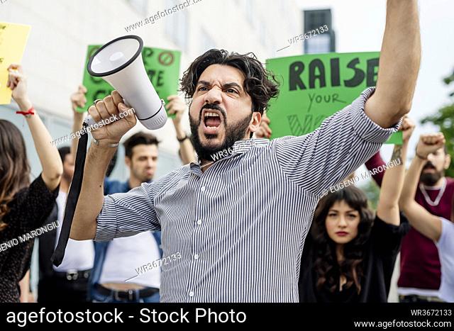 Man holding megaphone screaming with protestors on street
