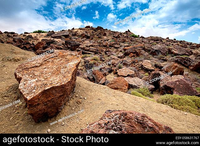 Dry deserted land of an abandoned copper mine with big rocks on the cliff and blue cloudy sky