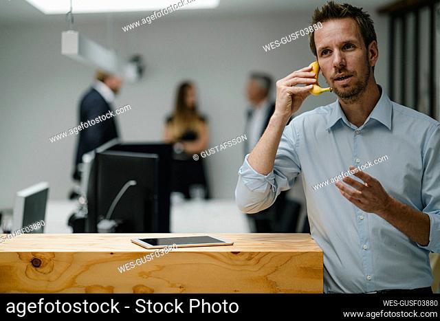 Businessman standing in open office door, using banana as a phone
