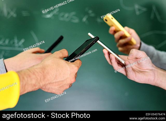Students using mobile phones in classroom with a chalkboard in the background