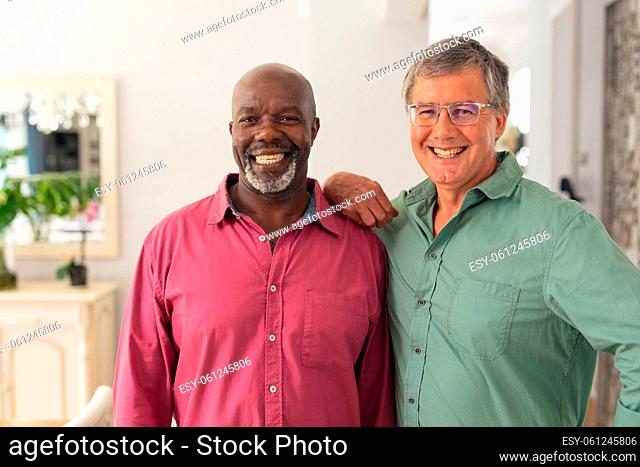 Portrait of smiling caucasian and african american senior male friends standing at home
