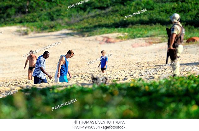 Mario Goetze (2nd L) walks on the beach in front of a soldier in Santo Andre, Brazil, 17 June 2014. The FIFA World Cup 2014 will take place in Brazil from 12...