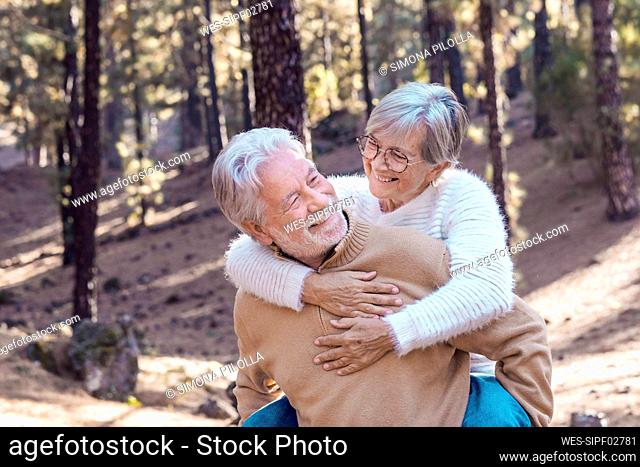 Happy senior man giving piggyback ride to woman in forest