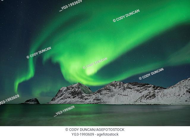 Aurora Borealis - Northern Lights shine in sky over snow covered mountains from Vik beach, Vestvågøy, Lofoten Islands, Norway