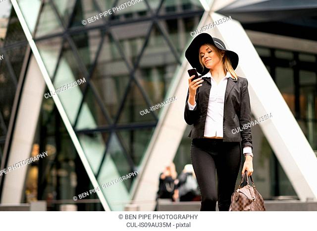 Woman texting while walking, 30 St Mary Axe in background, London, UK