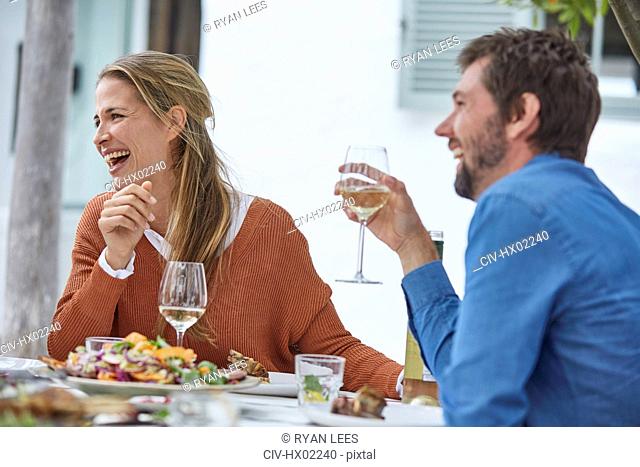 Laughing couple drinking white wine and eating lunch at patio table
