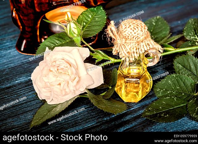 Essential rose oil on dark blue wooden background. Vintage toned effect