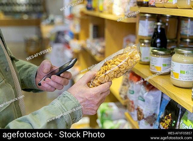 Close-up of senior man with smartphone buying groceries in a small food store checking ingredients