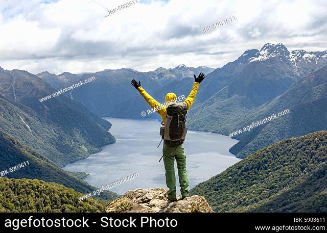 Mountaineer, hiker looks into the distance, stretching arms in the air, view of the South Fiord of Lake Te Anau, Murchison Mountains and Southern Alps in the...