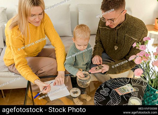 Parents with son counting coins in living room at home